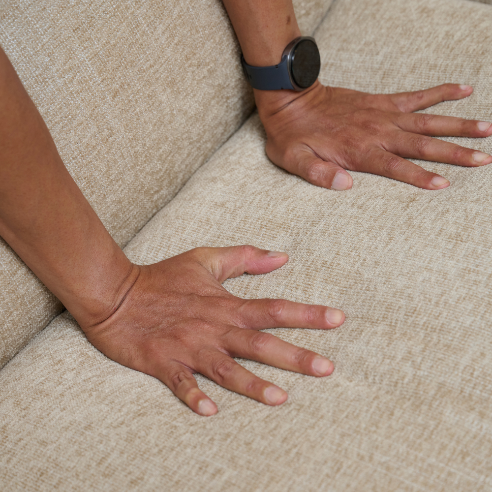 Close-up of a person's hands resting on the textured of ELLE Home Amelie Armchair Lemon Ultra-Soft Weave, with one hand wearing a dark smartwatch.
