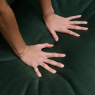 A close-up of a person's hands pressing down on ELLE Home Chloe Armchair Moss Green Velvet to show its soft texture and sheen.